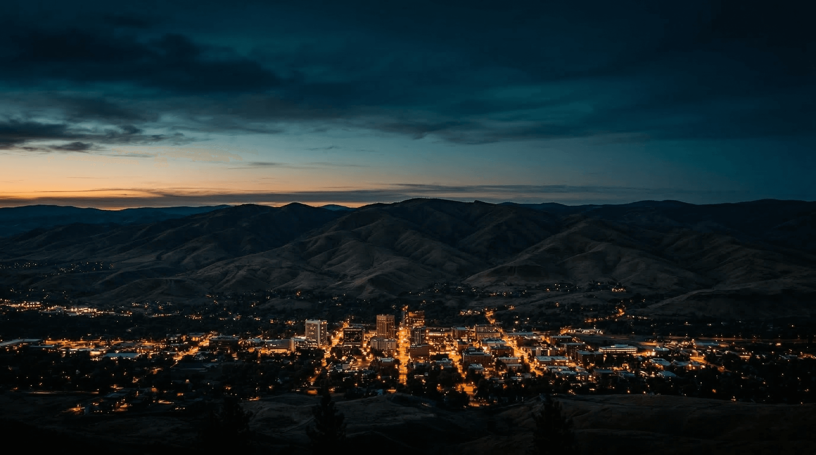 Boise Idaho skyline at blue hour with foothills rising behind the city and warm amber city lights